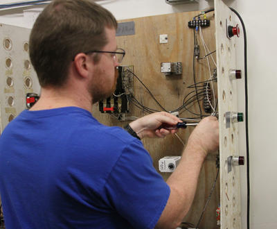 Electrical Student in Blue Shirt Installing Wire in Lab Setting