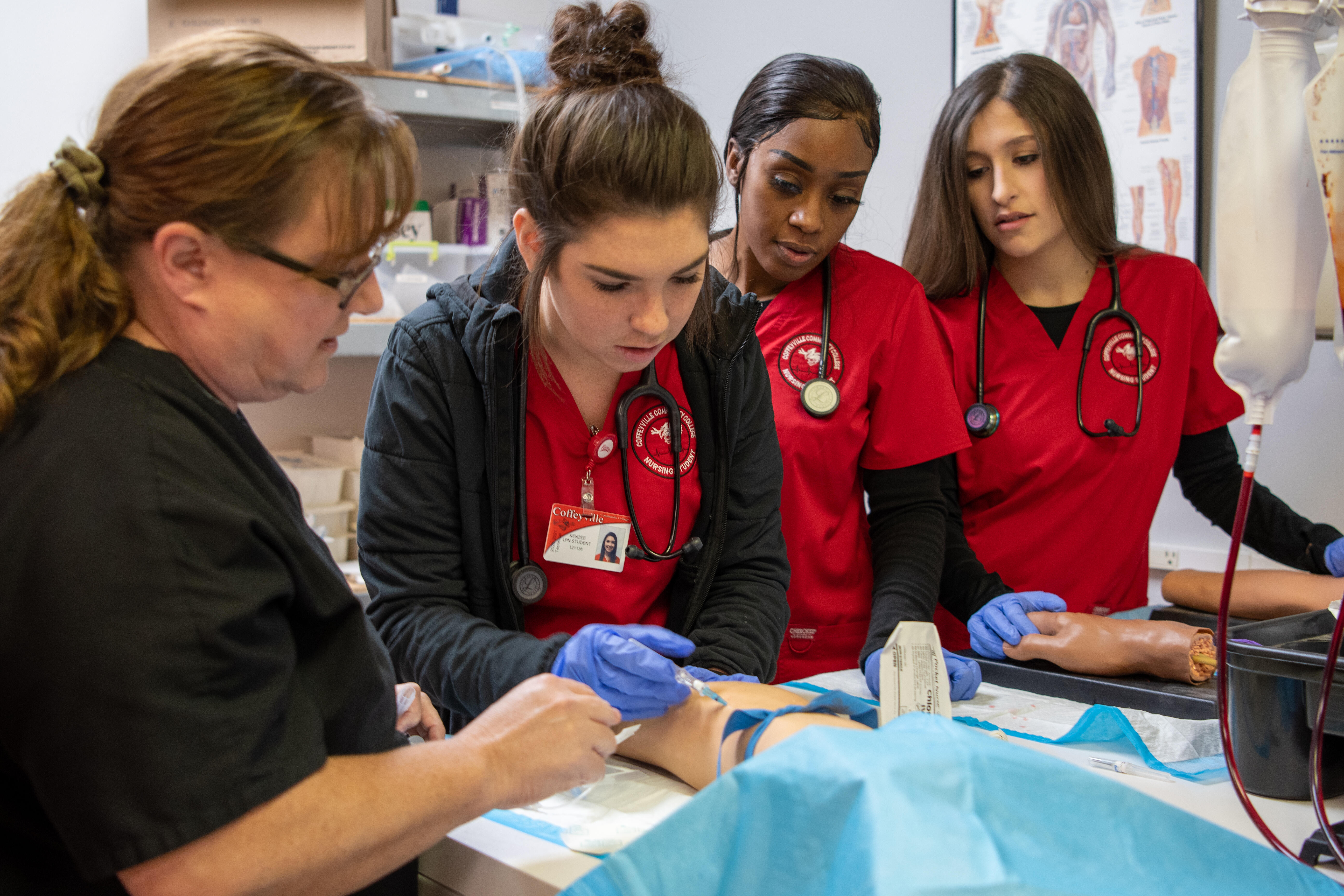 A nursing student and instructor practice taking blood on a dummy while two other student observe